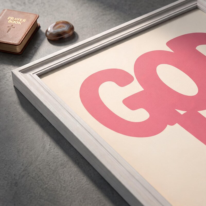 Angled close-up of the God Is Good pink poster showing rounded lettering on a cream background.