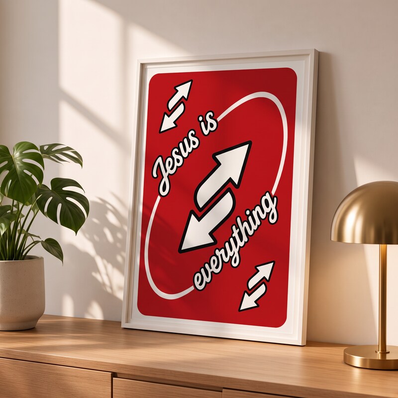 Jesus Is Everything red Christian poster in a styled tabletop mockup beside a plant and brass-colored lamp.