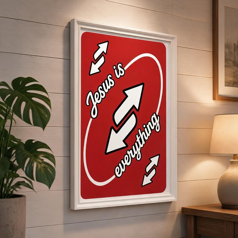 Jesus Is Everything red Christian poster displayed in a white frame on a paneled wall beside a plant and lamp.
