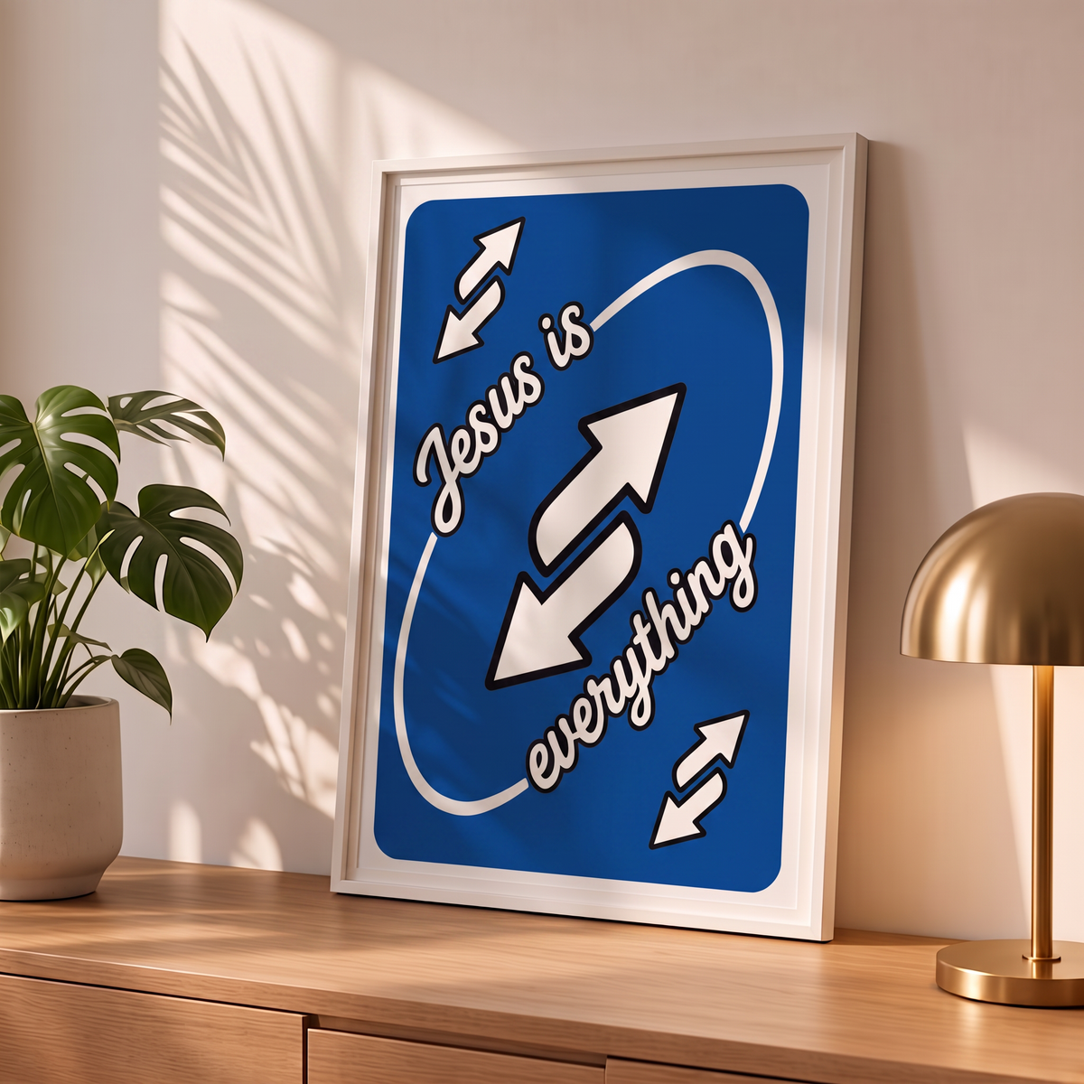 Jesus Is Everything blue Christian poster in a styled tabletop mockup beside a plant and brass-colored lamp.