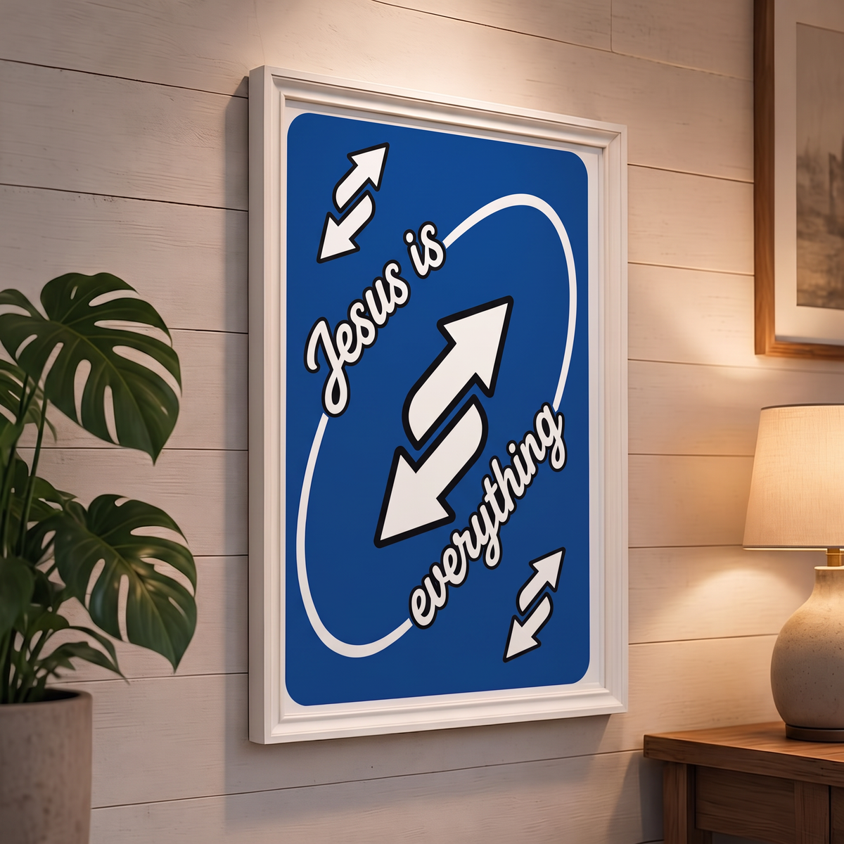 Jesus Is Everything blue Christian poster displayed in a white frame on a paneled wall beside a plant and lamp.