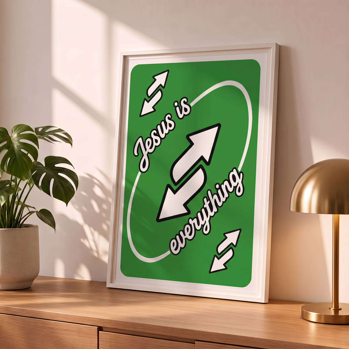 Jesus Is Everything green Christian poster in a styled tabletop mockup beside a plant and brass-colored lamp.