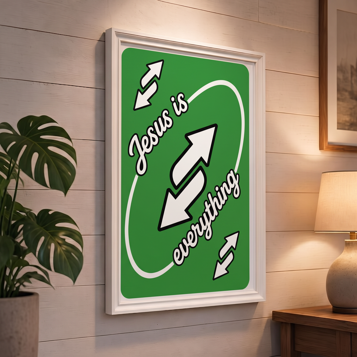 Jesus Is Everything green Christian poster displayed in a white frame on a paneled wall beside a plant and lamp.