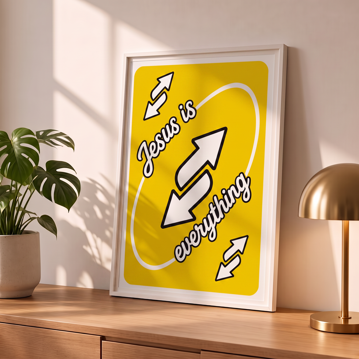 Jesus Is Everything yellow Christian poster in a styled tabletop mockup beside a plant and brass-colored lamp.