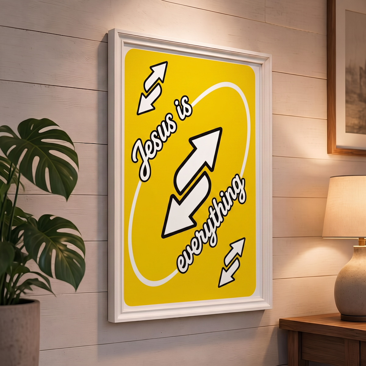 Jesus Is Everything yellow Christian poster displayed in a white frame on a paneled wall beside a plant and lamp.