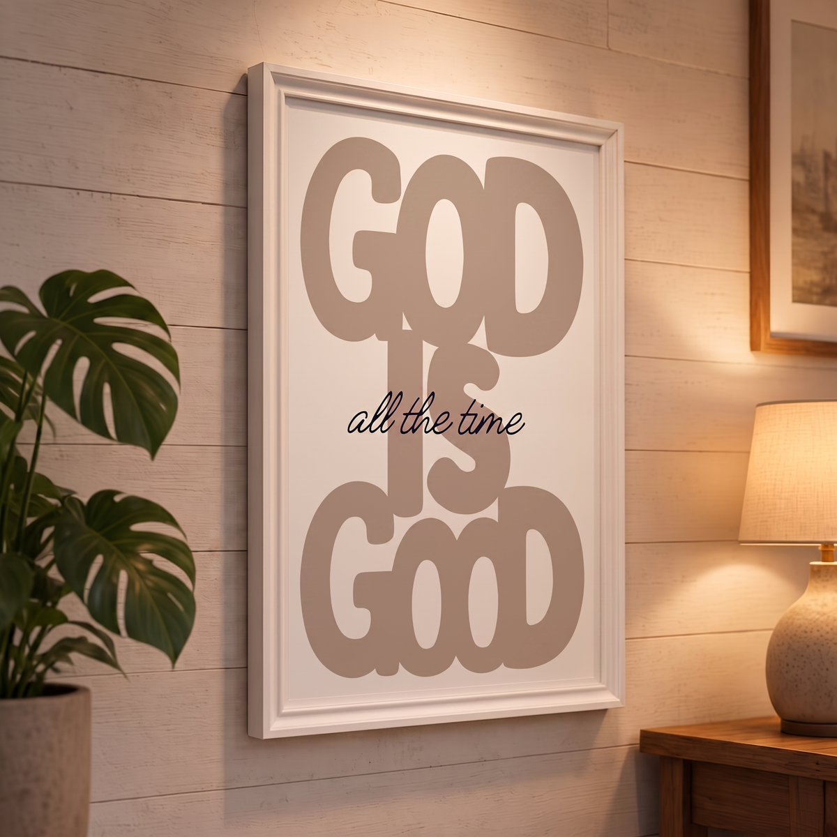 God Is Good brown Christian poster displayed in a white frame on a paneled wall beside a plant and lamp.