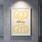 God Is Good yellow typography poster on cream, displayed in a white frame against a gray wall.
