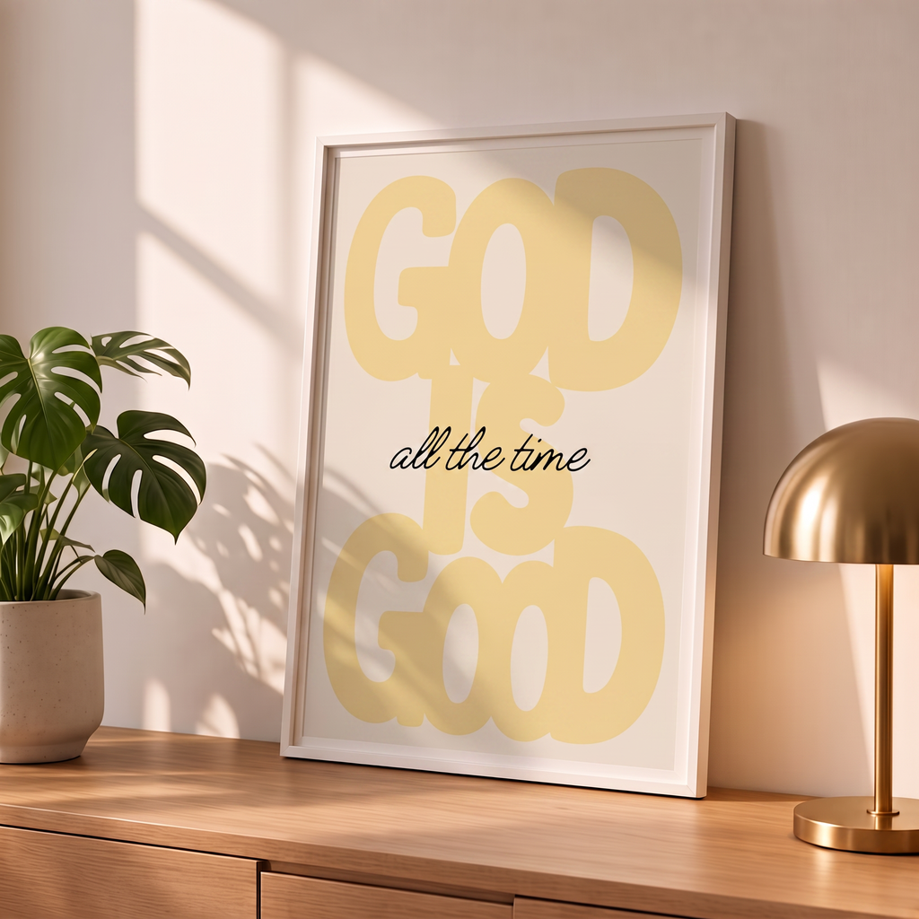 God Is Good yellow poster in a styled tabletop mockup beside a plant and brass-colored lamp.