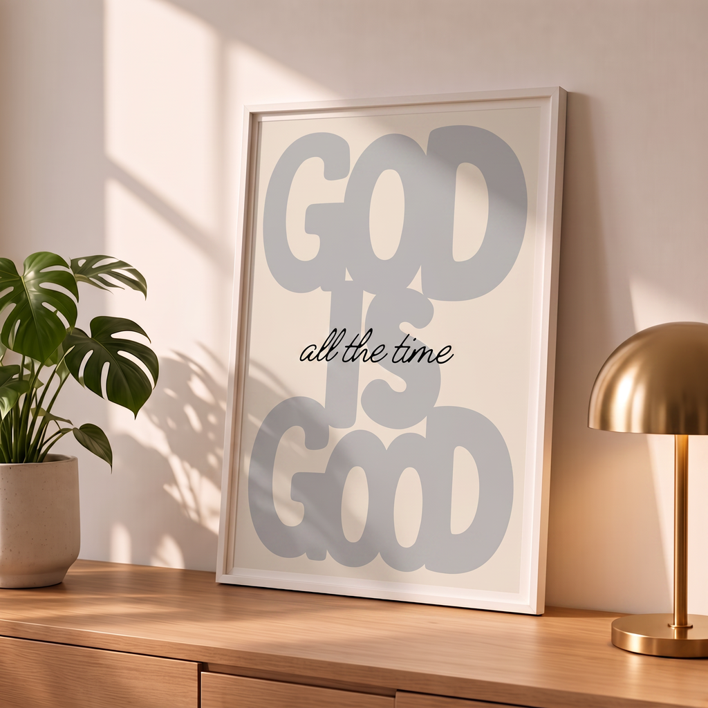 God Is Good grey Christian poster in a styled tabletop mockup beside a plant and brass-colored lamp.